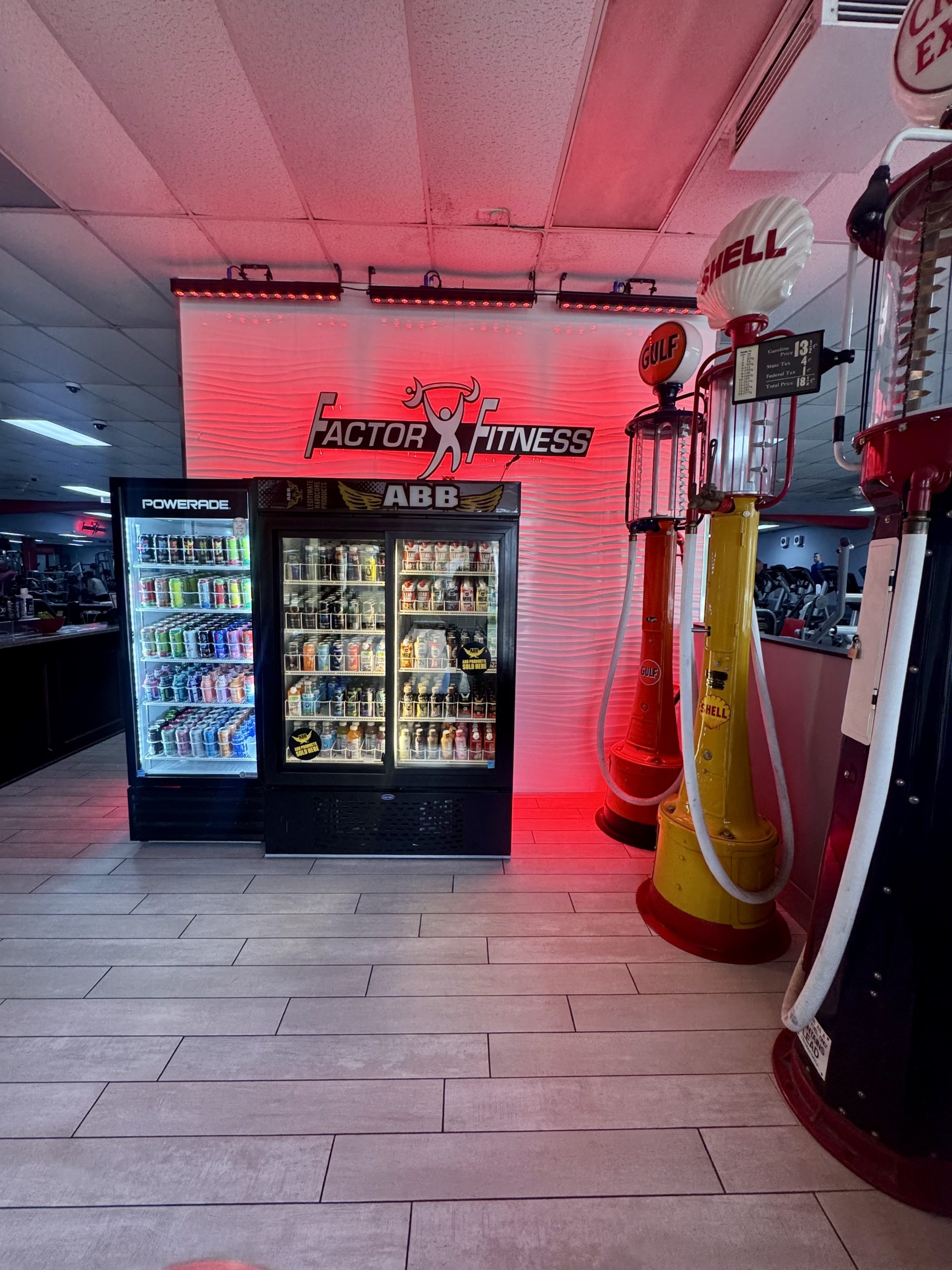 Image of fridges stocked with drinks. Red LED light is shining on the wall, and there are three vintage gas pumps for decor.