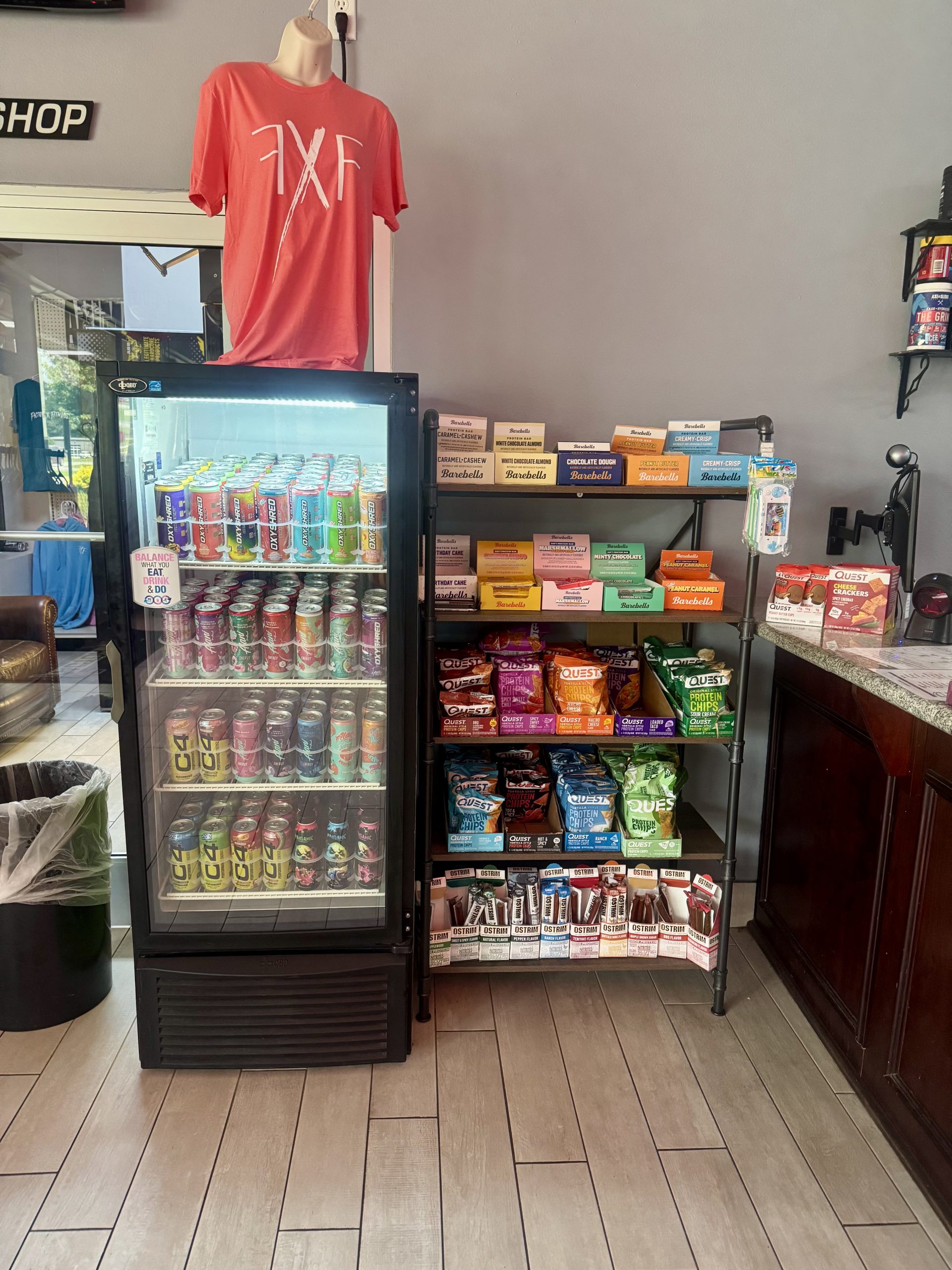 Image of shop floor. There are racks with shirts and fridges stocked with drinks.